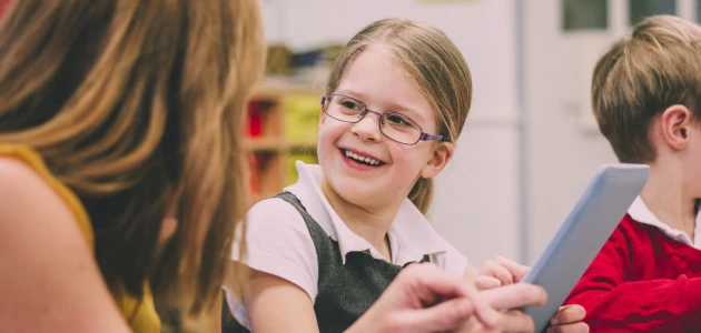 A picture pf a young girl with dyslexia using assistive technology and being supported by a teaching assistant